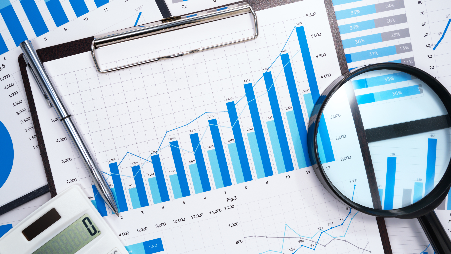 A magnifying glass hovers over a spread of charts and graphs.